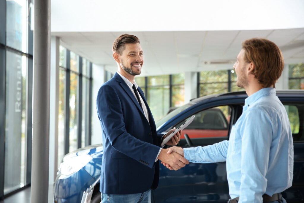 Men shaking hands in front of a car