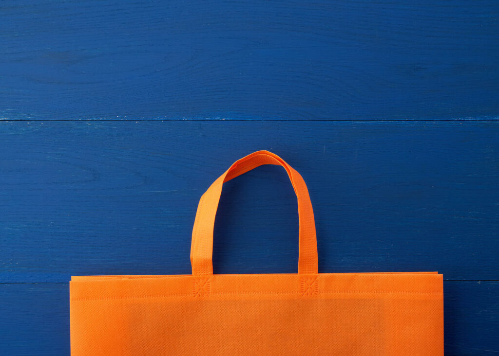 Reusable orange viscose bag on blue wooden background