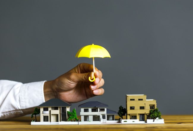 Hand holding little umbrella over homes