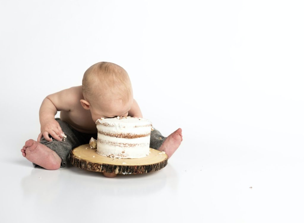A toddler sitting on the floor, smashing its face into a cake
