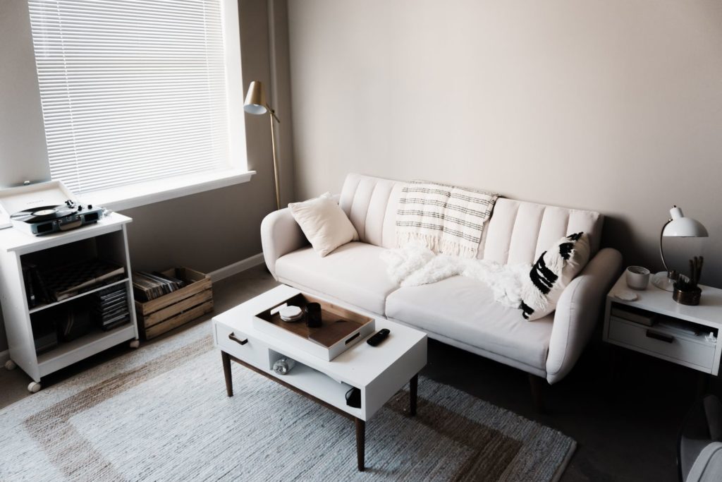 White sofa, white coffee table in front of it, white cabinet, and a window on the left 