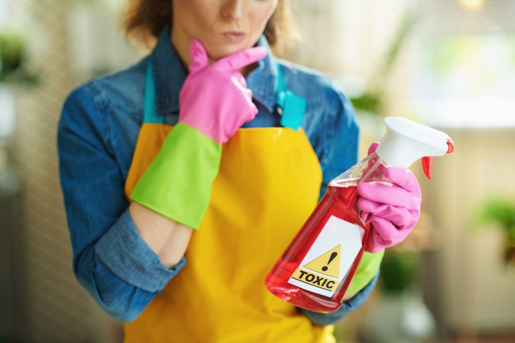 a woman looking at a cleaning liquid labeled as 'toxic'