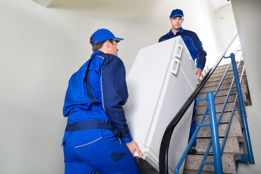 Two professional movers are carrying a refrigerator on the stairs