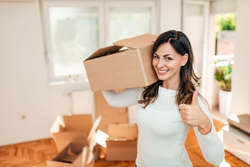 Happy young woman showing thumbs up while moving into new apartment.