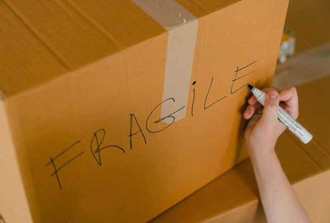 A person writing fragile on a box